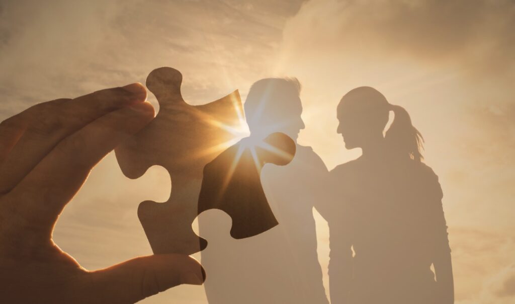 Holding up a puzzle piece with a couple's silhouette in the background 