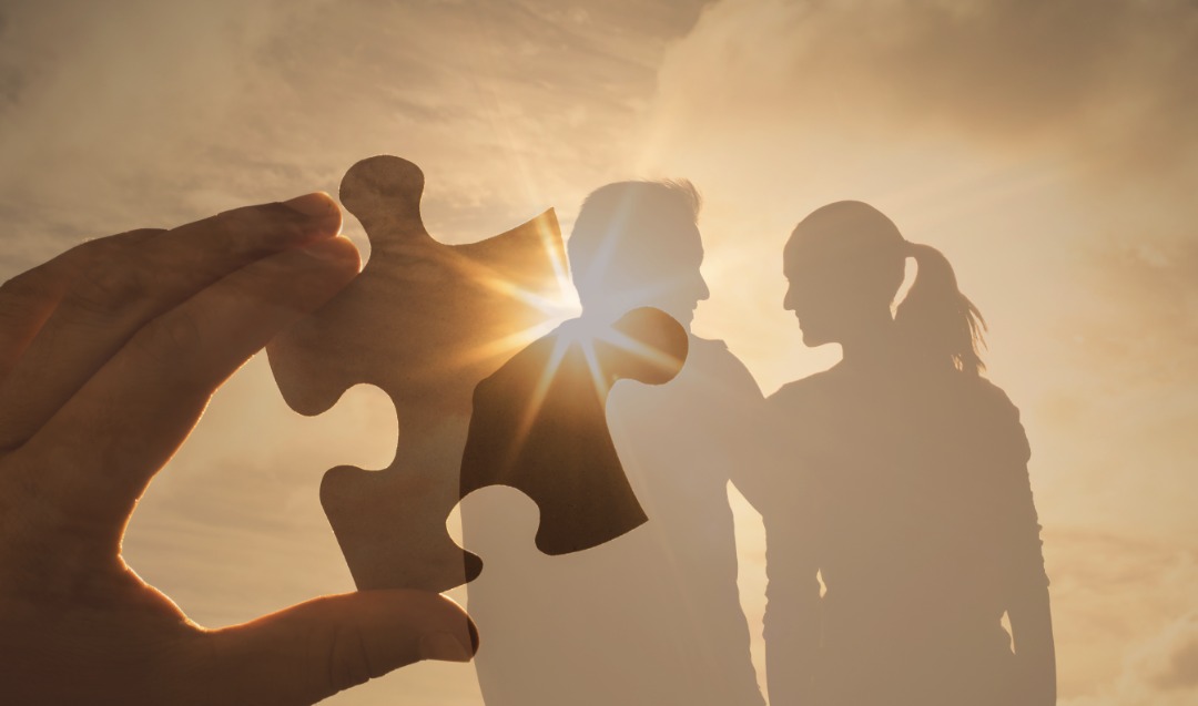 Holding up a puzzle piece with a couple's silhouette in the background